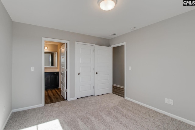 unfurnished bedroom featuring a closet, dark carpet, connected bathroom, and baseboards