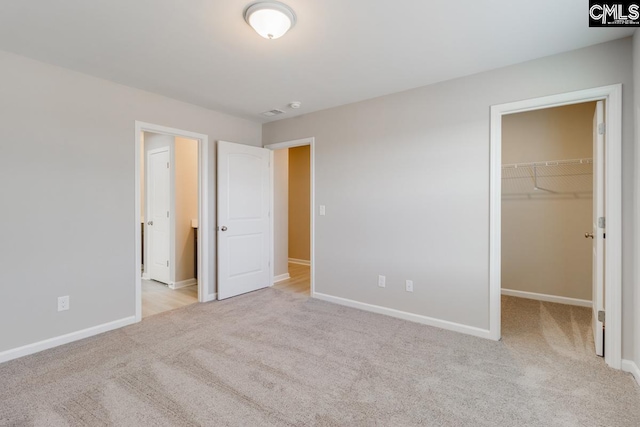 unfurnished bedroom with baseboards, a walk in closet, and carpet flooring