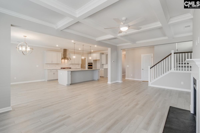 unfurnished living room with stairs, ceiling fan with notable chandelier, coffered ceiling, and light wood-style flooring