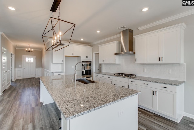 kitchen with white cabinets, wainscoting, wood finished floors, stainless steel appliances, and wall chimney range hood