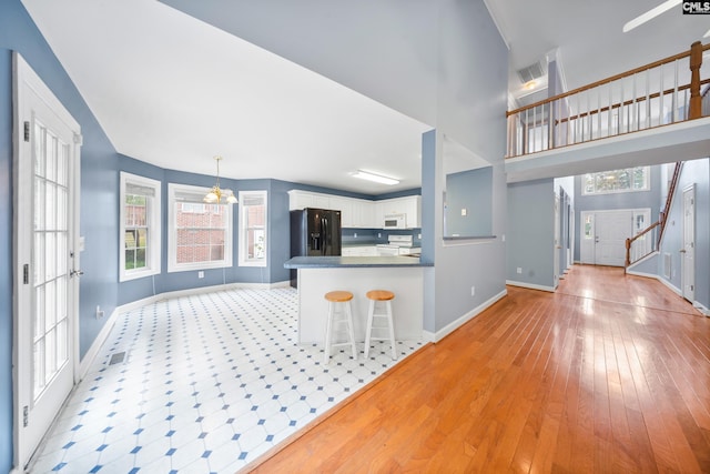 kitchen with white cabinets, kitchen peninsula, hanging light fixtures, light hardwood / wood-style flooring, and white appliances