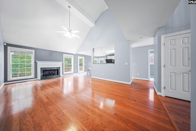 unfurnished living room featuring light wood-type flooring, high vaulted ceiling, a premium fireplace, beamed ceiling, and ceiling fan