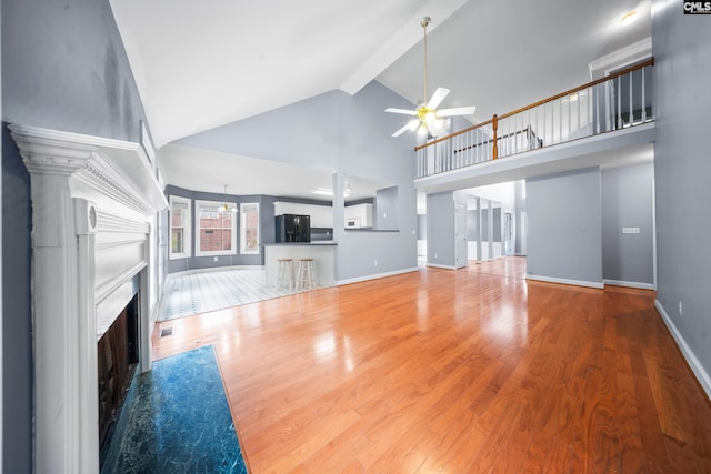 unfurnished living room featuring high vaulted ceiling, hardwood / wood-style floors, ceiling fan, and beam ceiling