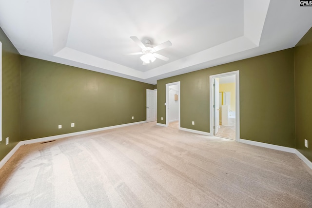 unfurnished bedroom featuring ensuite bathroom, light carpet, ceiling fan, and a tray ceiling