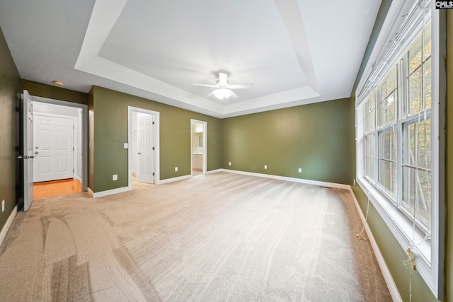 unfurnished bedroom featuring ensuite bathroom, light colored carpet, ceiling fan, and a tray ceiling