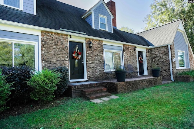 view of front of house with brick siding, a chimney, a front lawn, and roof with shingles