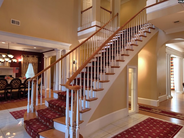 stairway with ornate columns, wood-type flooring, a towering ceiling, a chandelier, and ornamental molding