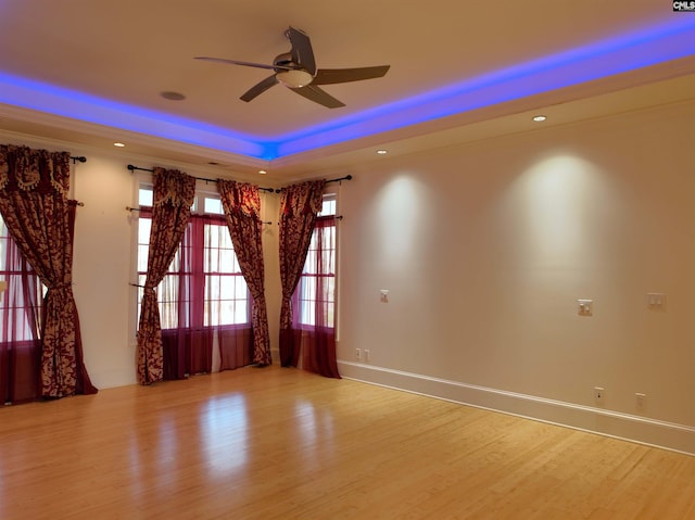 spare room with light hardwood / wood-style floors, ceiling fan, ornamental molding, and a tray ceiling