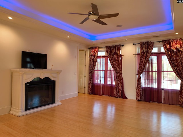 unfurnished living room with light hardwood / wood-style floors, a raised ceiling, and a wealth of natural light