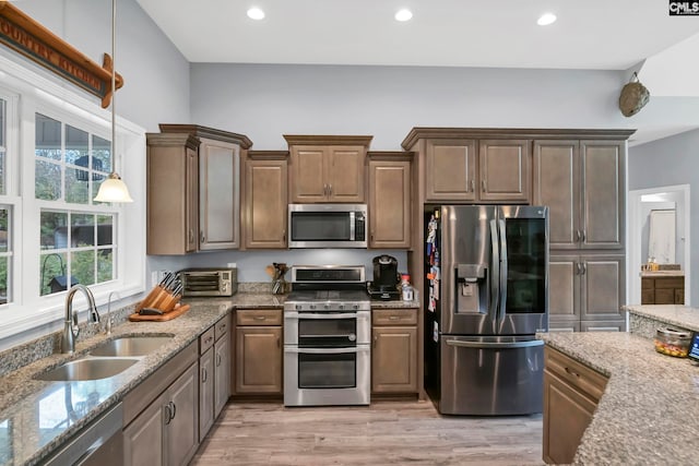 kitchen featuring sink, appliances with stainless steel finishes, light stone countertops, hanging light fixtures, and light hardwood / wood-style flooring