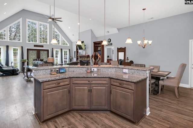 kitchen with ceiling fan with notable chandelier, decorative light fixtures, high vaulted ceiling, an island with sink, and dark hardwood / wood-style flooring