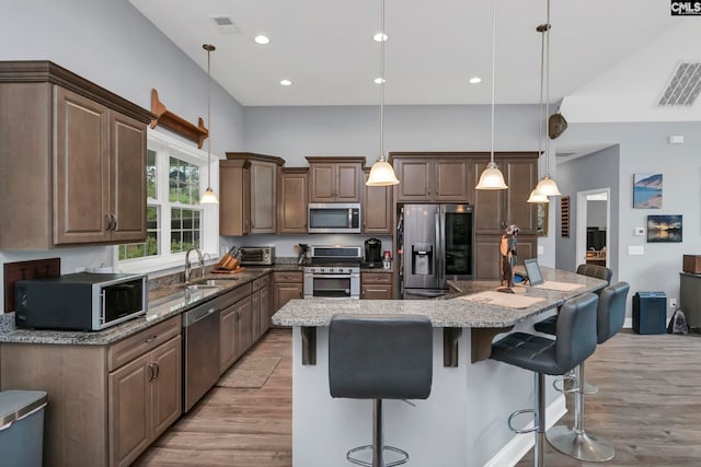 kitchen featuring stainless steel appliances, light hardwood / wood-style floors, a center island, decorative light fixtures, and dark stone countertops