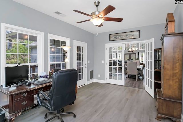 office with french doors, ceiling fan with notable chandelier, and light hardwood / wood-style flooring