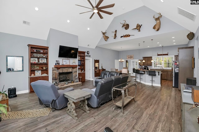 living room with dark hardwood / wood-style flooring, high vaulted ceiling, a stone fireplace, and ceiling fan with notable chandelier