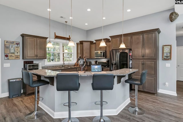 kitchen featuring stainless steel appliances, a breakfast bar, light stone counters, a kitchen island, and pendant lighting