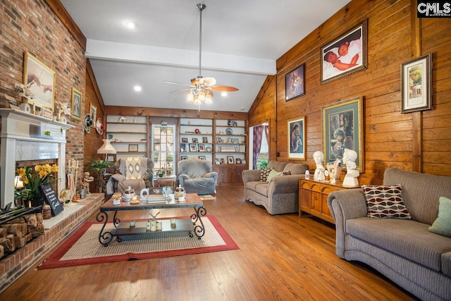 living room with wooden walls, ceiling fan, beam ceiling, a fireplace, and light hardwood / wood-style flooring