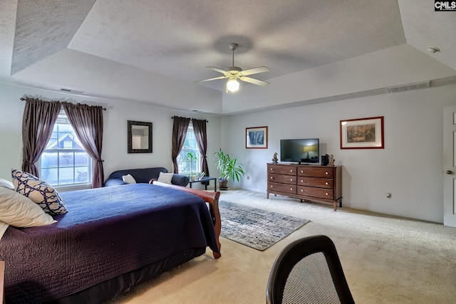 carpeted bedroom with a textured ceiling, ceiling fan, and a raised ceiling