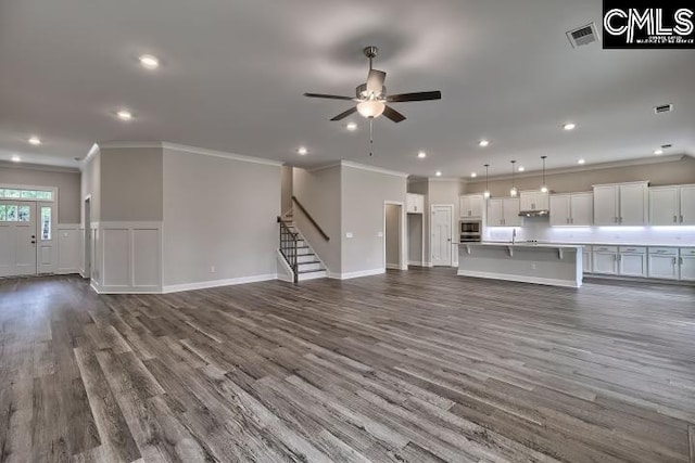 unfurnished living room with ceiling fan, ornamental molding, and dark wood-type flooring