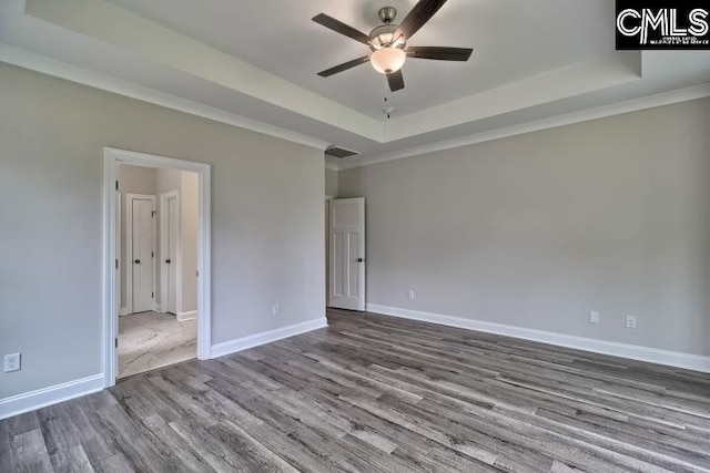 empty room with a tray ceiling, ceiling fan, ornamental molding, and hardwood / wood-style flooring