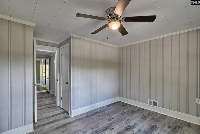 unfurnished room with light hardwood / wood-style floors, ceiling fan, wooden walls, and crown molding