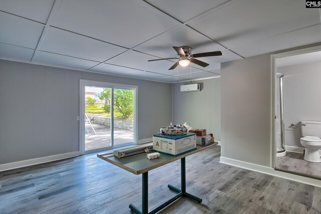 interior space with a drop ceiling, a wall mounted AC, wood walls, hardwood / wood-style flooring, and ceiling fan