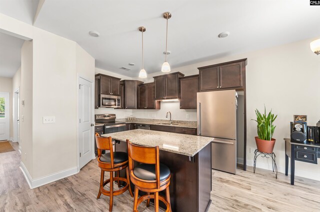 kitchen with pendant lighting, light wood-type flooring, appliances with stainless steel finishes, and light stone countertops