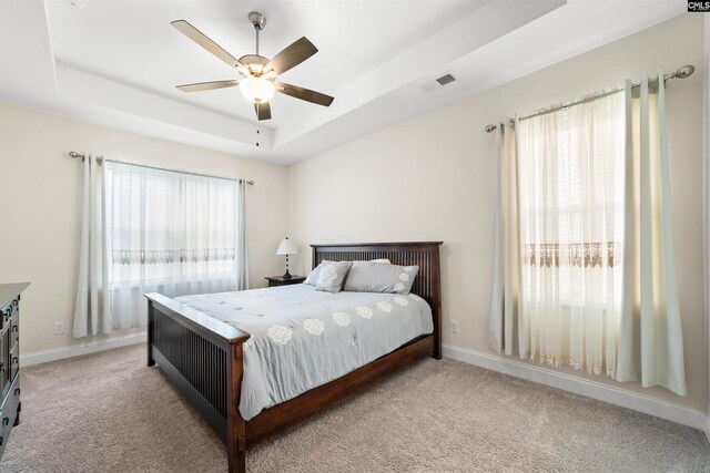 bedroom with ceiling fan, multiple windows, light carpet, and a tray ceiling