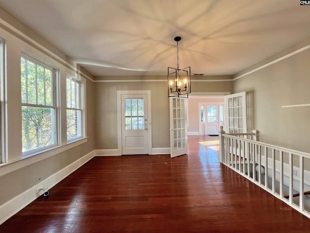 unfurnished dining area featuring french doors, dark hardwood / wood-style floors, a chandelier, and crown molding