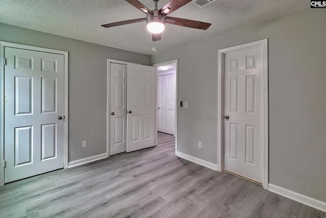 unfurnished bedroom featuring light hardwood / wood-style floors, ceiling fan, a textured ceiling, and two closets