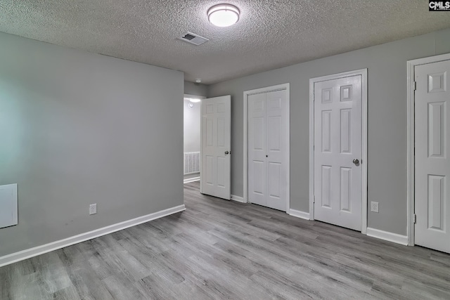 unfurnished bedroom featuring multiple closets, a textured ceiling, and light hardwood / wood-style flooring