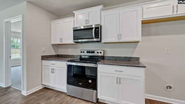 kitchen with dark stone countertops, white cabinetry, light hardwood / wood-style floors, and appliances with stainless steel finishes