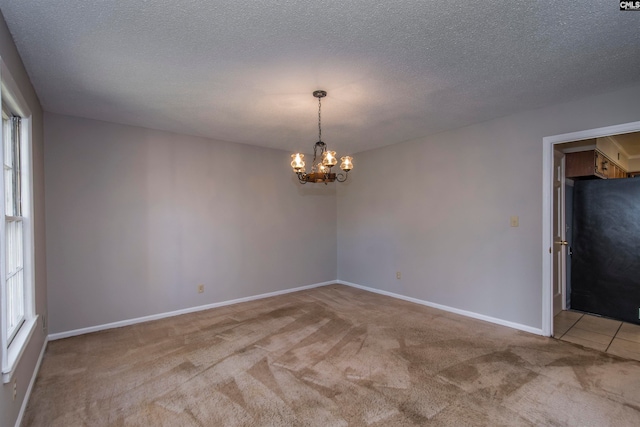 carpeted empty room with a textured ceiling, plenty of natural light, and a chandelier