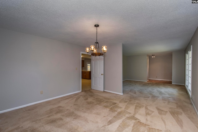 carpeted spare room featuring a textured ceiling and an inviting chandelier