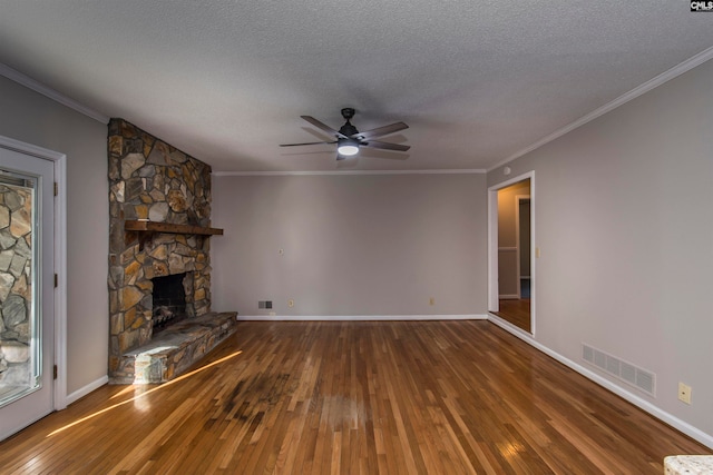 unfurnished living room featuring ceiling fan, a textured ceiling, wood-type flooring, a stone fireplace, and crown molding