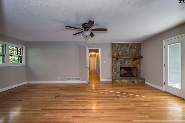 unfurnished living room with a stone fireplace, light wood-type flooring, and a textured ceiling