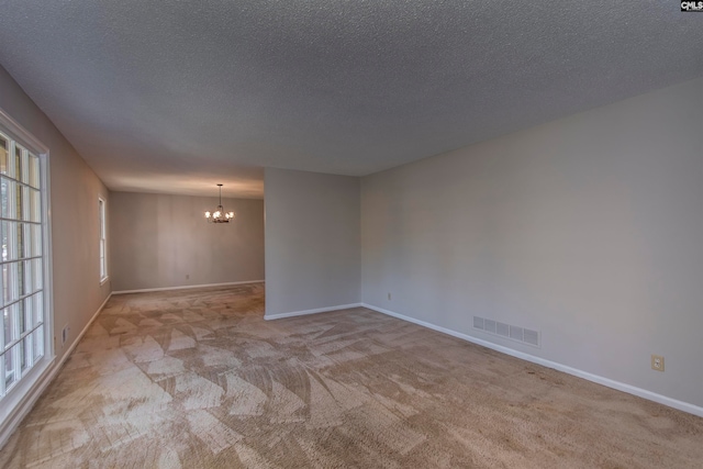 carpeted empty room with a chandelier and a textured ceiling