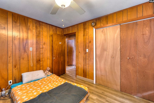 bedroom with light hardwood / wood-style floors, ceiling fan, a textured ceiling, and wooden walls