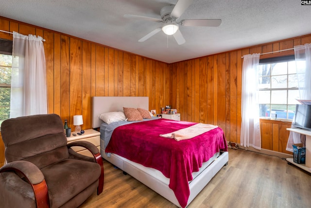 bedroom featuring wood walls, hardwood / wood-style floors, ceiling fan, and a textured ceiling