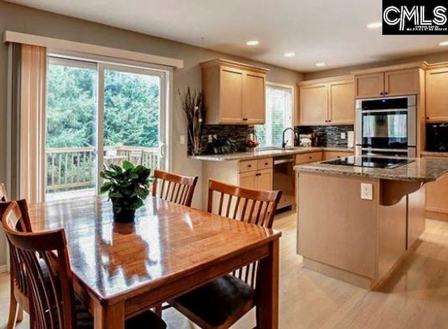 kitchen with light brown cabinetry, light stone counters, a center island, and black appliances