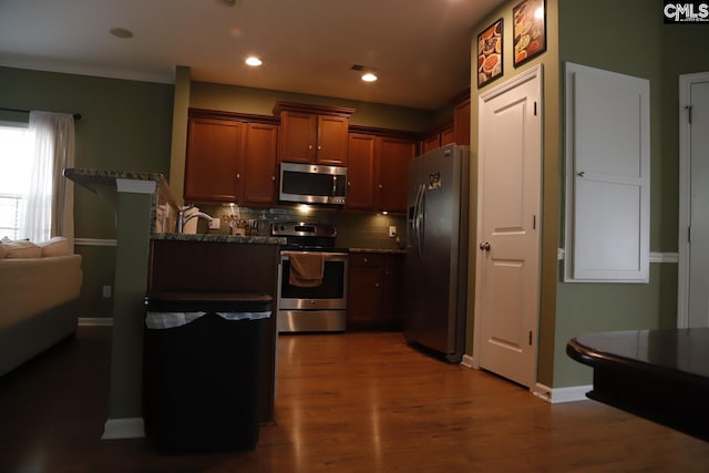 kitchen with decorative backsplash, appliances with stainless steel finishes, dark stone countertops, crown molding, and dark hardwood / wood-style flooring