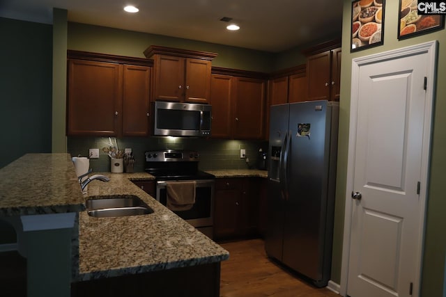 kitchen featuring stainless steel appliances, hardwood / wood-style flooring, sink, kitchen peninsula, and tasteful backsplash