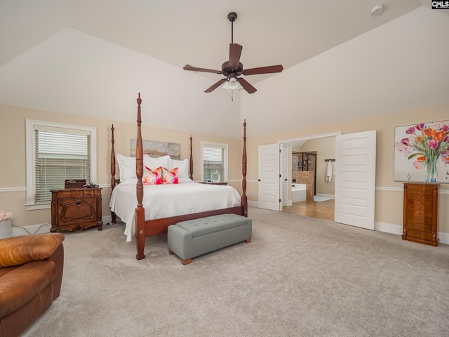 carpeted bedroom with ensuite bathroom, multiple windows, ceiling fan, and high vaulted ceiling