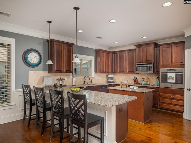 kitchen featuring a wealth of natural light, appliances with stainless steel finishes, decorative light fixtures, and a kitchen breakfast bar