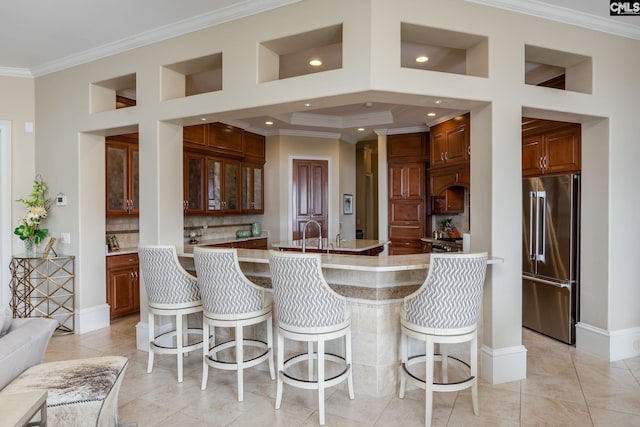 kitchen featuring high end refrigerator, ornamental molding, tasteful backsplash, a kitchen bar, and light tile patterned floors