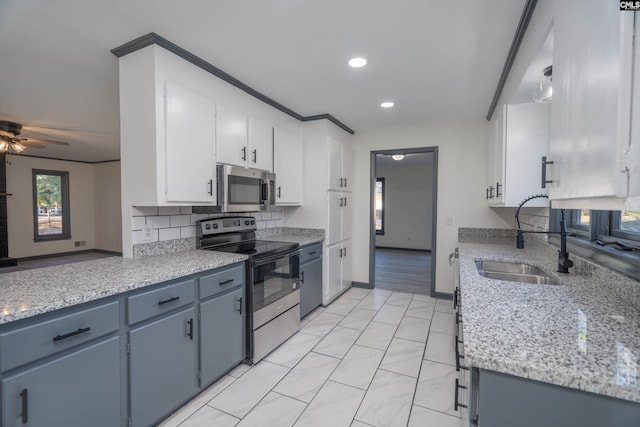 kitchen with sink, light stone counters, appliances with stainless steel finishes, blue cabinetry, and white cabinets