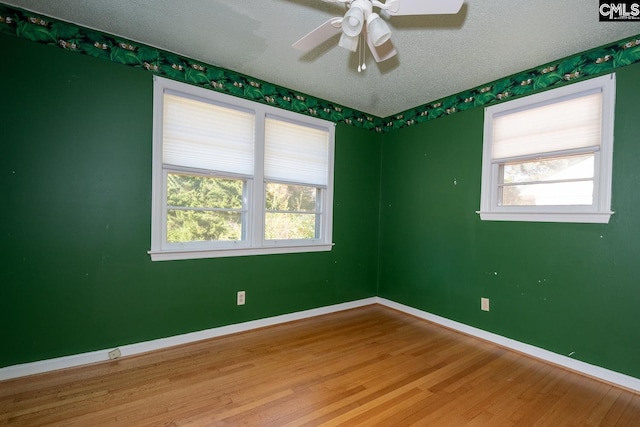 empty room featuring ceiling fan, wood-type flooring, a healthy amount of sunlight, and a textured ceiling