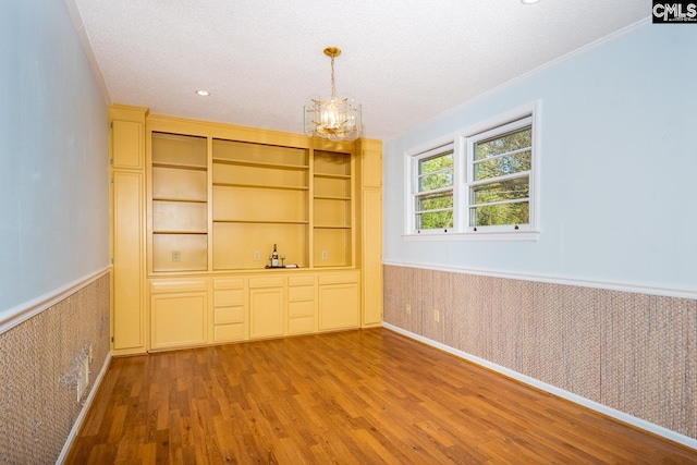 interior space featuring a textured ceiling, hardwood / wood-style floors, a chandelier, and crown molding