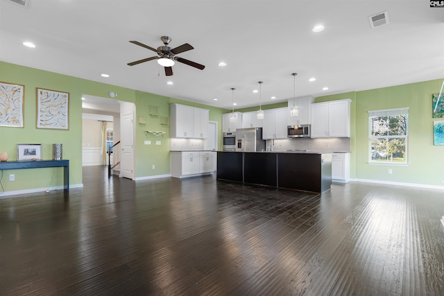 kitchen with dark wood-type flooring, a center island with sink, white cabinets, pendant lighting, and appliances with stainless steel finishes