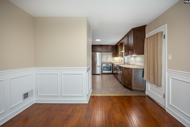 kitchen with sink, light stone counters, dark brown cabinets, appliances with stainless steel finishes, and hardwood / wood-style flooring