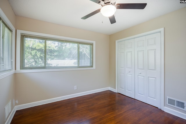 unfurnished bedroom with a closet, ceiling fan, multiple windows, and dark hardwood / wood-style floors